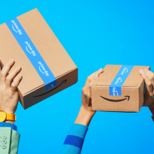 hands holding up Amazon Prime packages against blue background