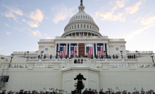 The United States Marine Band rehearsing their performance in front of the Capitol building, as large American flags drape across the facade.