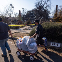 People pull a wagon of items through a neighborhood where many homes were destroyed by the Eaton Fire on January 11, 2025 in Altadena, California