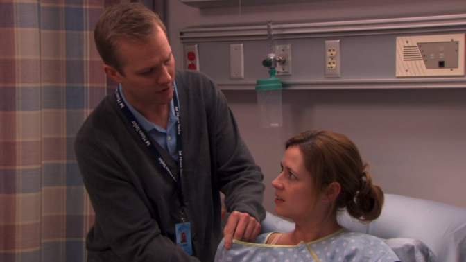 A male lactation nurse helping a woman who's sitting in a hospital bed.