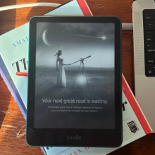 A Kindle Paperwhite on top of a stack of books.