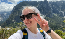 woman wearing sunglasses holding up a peace sign with mountains in the background