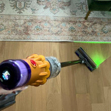 Person holding Dyson V12 Detect Slim to clean hardwood floor with laser on