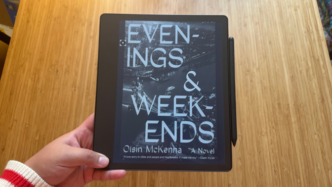 A person holding the Kindle Scribe showing the book cover of 'Evenings & Weekends'