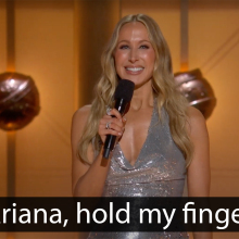 A woman stands on an award show stage. The caption at the bottom reads, "Ariana, hold my finger."