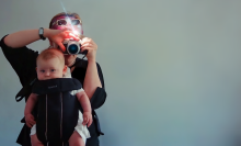 Still from 'Motherboard' shows Victoria Mapplebeck holding her baby son Jim in a sling carrier while she holds a camera to photograph them.