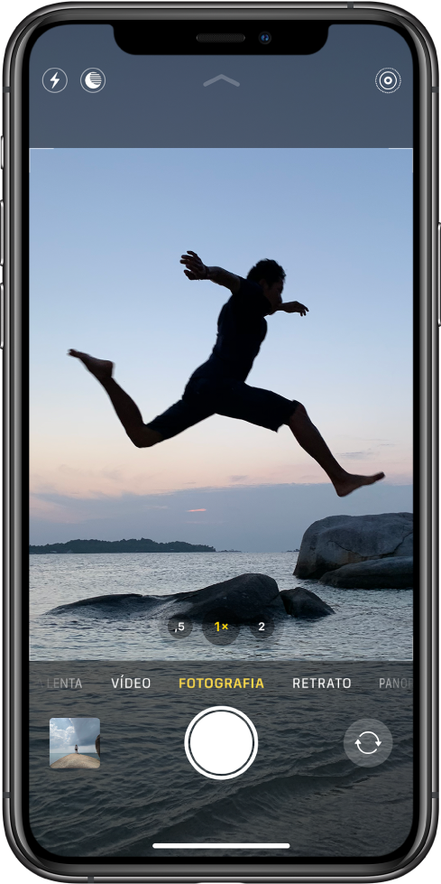 Ecrã da câmara em modo Fotografia, com os outros modos visíveis de cada lado por baixo do visor. Botões para o flash, modo noturno e Live Photo na parte superior do ecrã. Por baixo dos modos da câmara, da esquerda para a direita, uma miniatura de imagem para aceder a fotografias e vídeos, o botão do obturador e o botão para mudar de câmara.