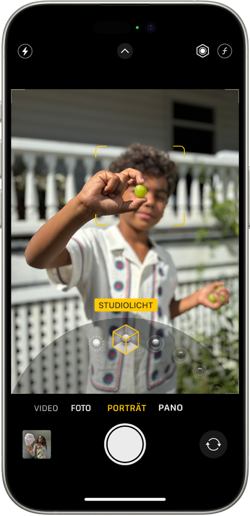 Der Bildschirm „Kamera“ im Modus „Porträt“. Das Motiv im Sucher ist scharf und der Hintergrund weichgezeichnet. Der Regler zum Auswählen der Porträtlichteffekte ist unten im Rahmen geöffnet und „Studiolicht“ ist ausgewählt. Oben links befindet sich die Taste „Blitz“, oben in der Mitte ist die Taste „Kamerasteuerung“ zu sehen und oben rechts befinden sich Tasten zum Anpassen der Intensität des Porträtlichts und der Tiefensteuerung. Unten auf dem Bildschirm sind von links nach rechts folgende Tasten zu sehen: „Foto- und Videoübersicht“, „Bild aufnehmen“ und „Kameraauswahl – rückseitige Kamera“.
