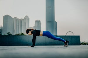 confidence and energetic young asian sports woman exercising and working out outdoors in urban park against city skyline at sunset