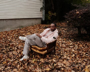 a person seated on a vintage armchair surrounded by fallen leaves in an outdoor setting