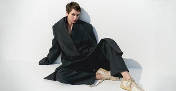 fashion model in oversized suit and sneakers seated against a white backdrop