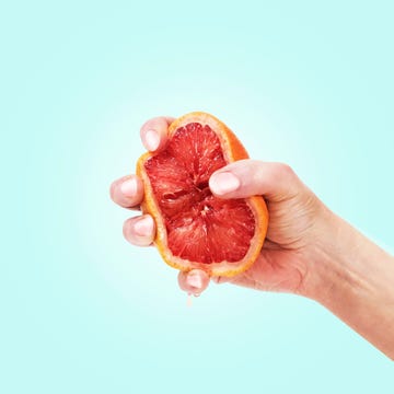 womans hand squeezing a grapefruit half on a blue background