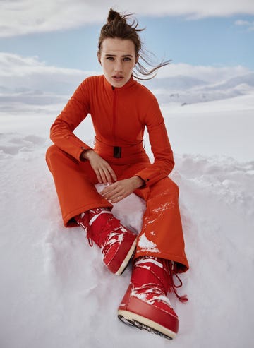 individual seated in a snowy landscape wearing an orange outfit and red snow boots for best designer snow boots