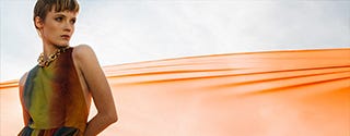 a person in a colorful dress stands against a backdrop of flowing orange fabric