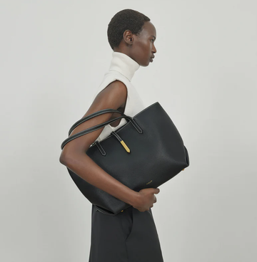 a model holding a large black tote bag with gold accents