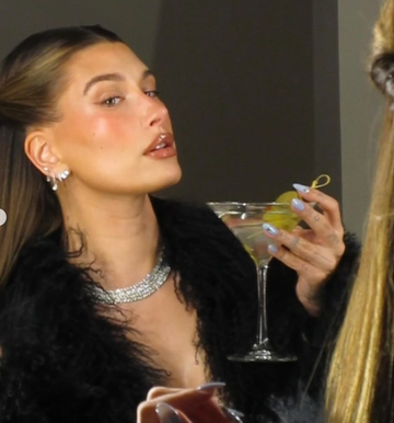 person holding a martini glass with a lemon twist and wearing a statement necklace