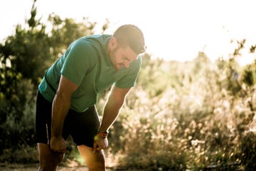 tired male runner bending in forest