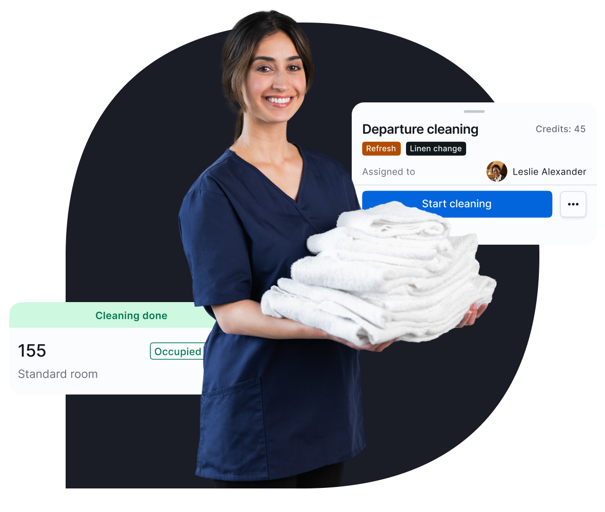 Smiling female housekeeping staff member holding a stack of folded white towels, with a task management interface overlay showing 'Departure cleaning statistics' and 'Cleaning done' for the room 155