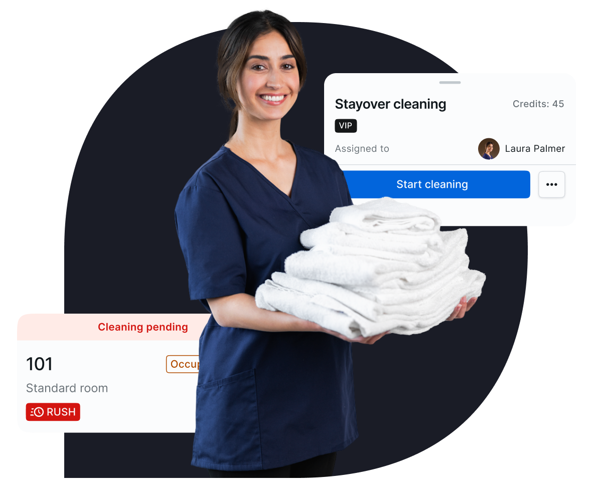 Smiling female housekeeping staff member holding a stack of folded white towels, with a task management interface overlay showing 'Stayover cleaning' and 'Cleaning pending' for room 101 marked as a rush task.