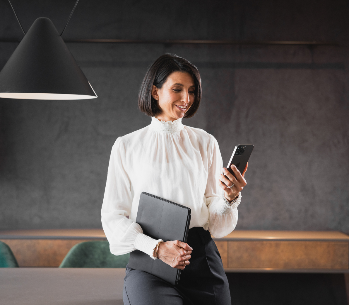 Smiling female hotel manager holding a folder, looking at her smartphone.