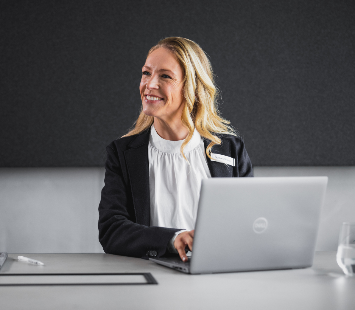 Smiling HR professional in a black blazer sitting with a laptop.