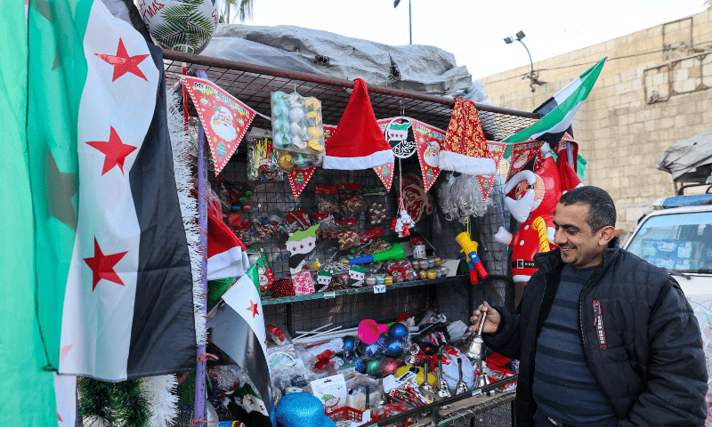 A street vendor shows his wares next his stand, adorned with independence-era Syria flags, in the Bab Touma neighbourhood in Damaascus on Dec 23, 2024. — AFP