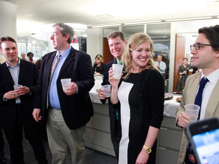 Reporters in a brightly lit room cheerfully holding drinks in plastic cups after being awarded the Pulitzer Prize.