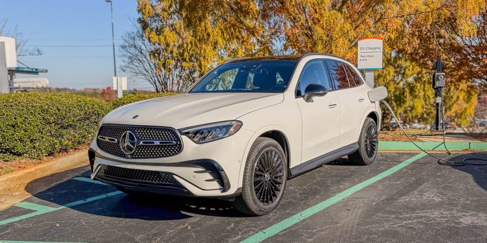 The left front corner of a white 2025 Mercedes-Benz GLC 350e Plug-in Hybrid SUV plugged into a charger.