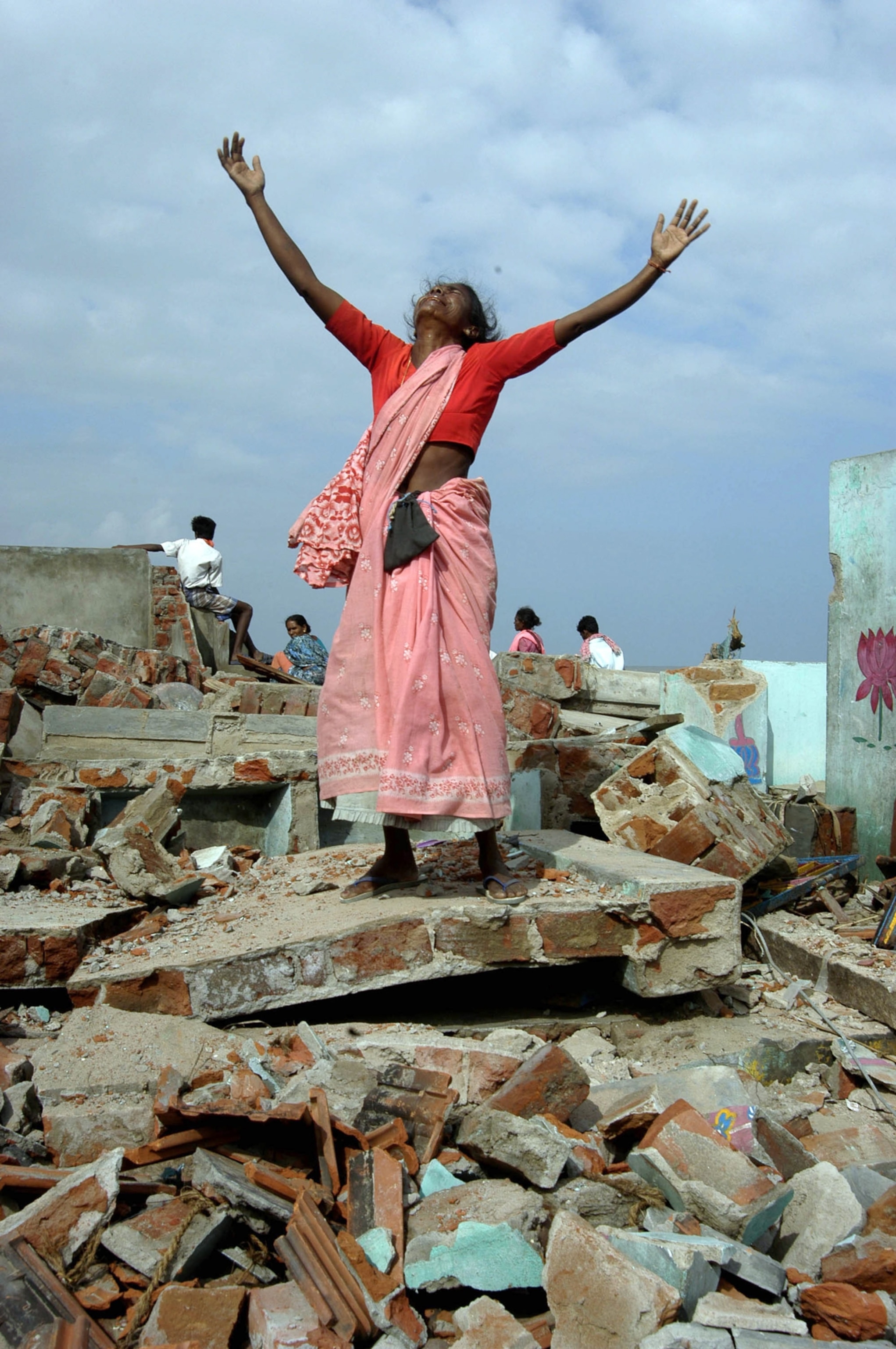 A woman dark skin reaches up to the sky while standing on ruble.