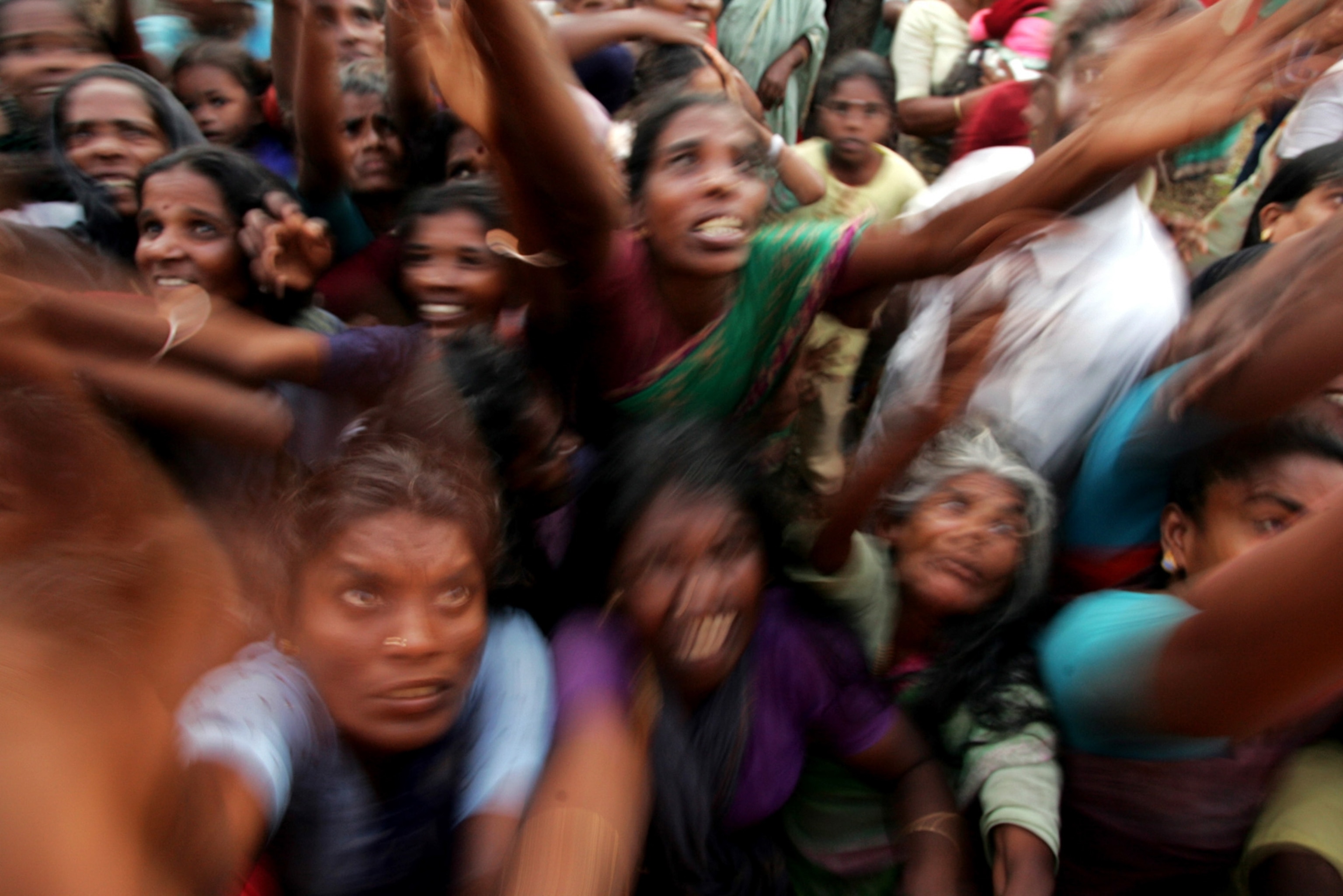 A crowd of people are close together reach upward with the hopes of obtaining aid.