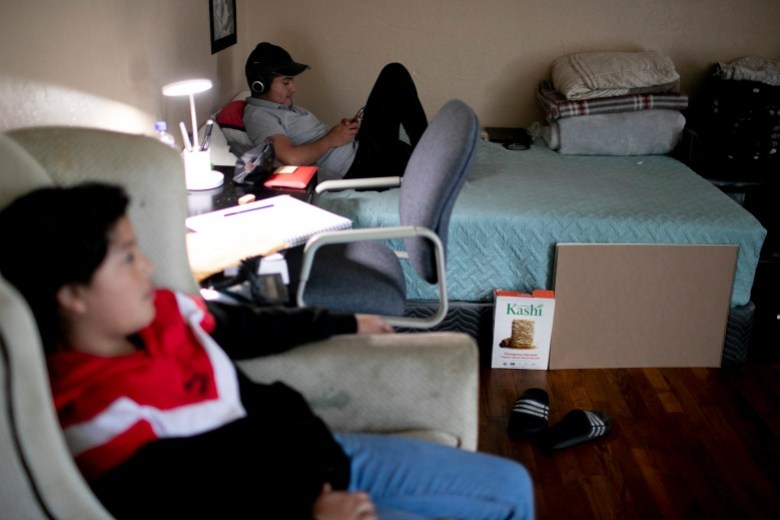 Eduardo se sienta en su cama mientras revisa su teléfono en la sala de la casa que comparte con sus hermanos y sobrinas. Foto de Anne Wernikoff, CalMatters