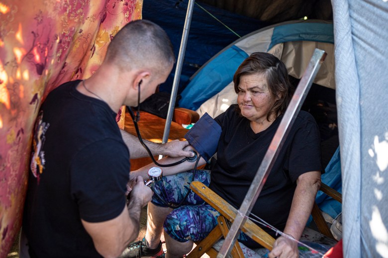 Physician's assistant Brett Feldman checks his patient, Carla Bolen’s, blood pressure while in her encampment at the Figueroa St. Viaduct above Highway 110 in Elysian Valley Park in Los Angeles on Nov. 18, 2022.Photo by Larry Valenzuela for CalMatters