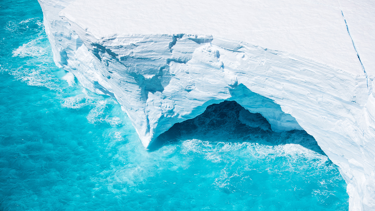 An iceberg in bright blue water, seen from above