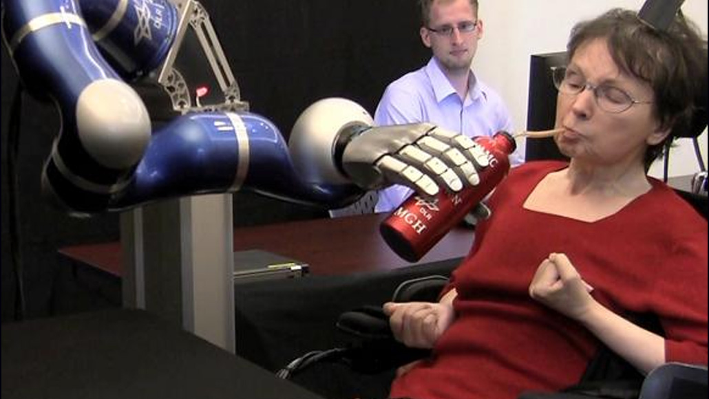 a woman drinks from a water bottle held by a robotic arm