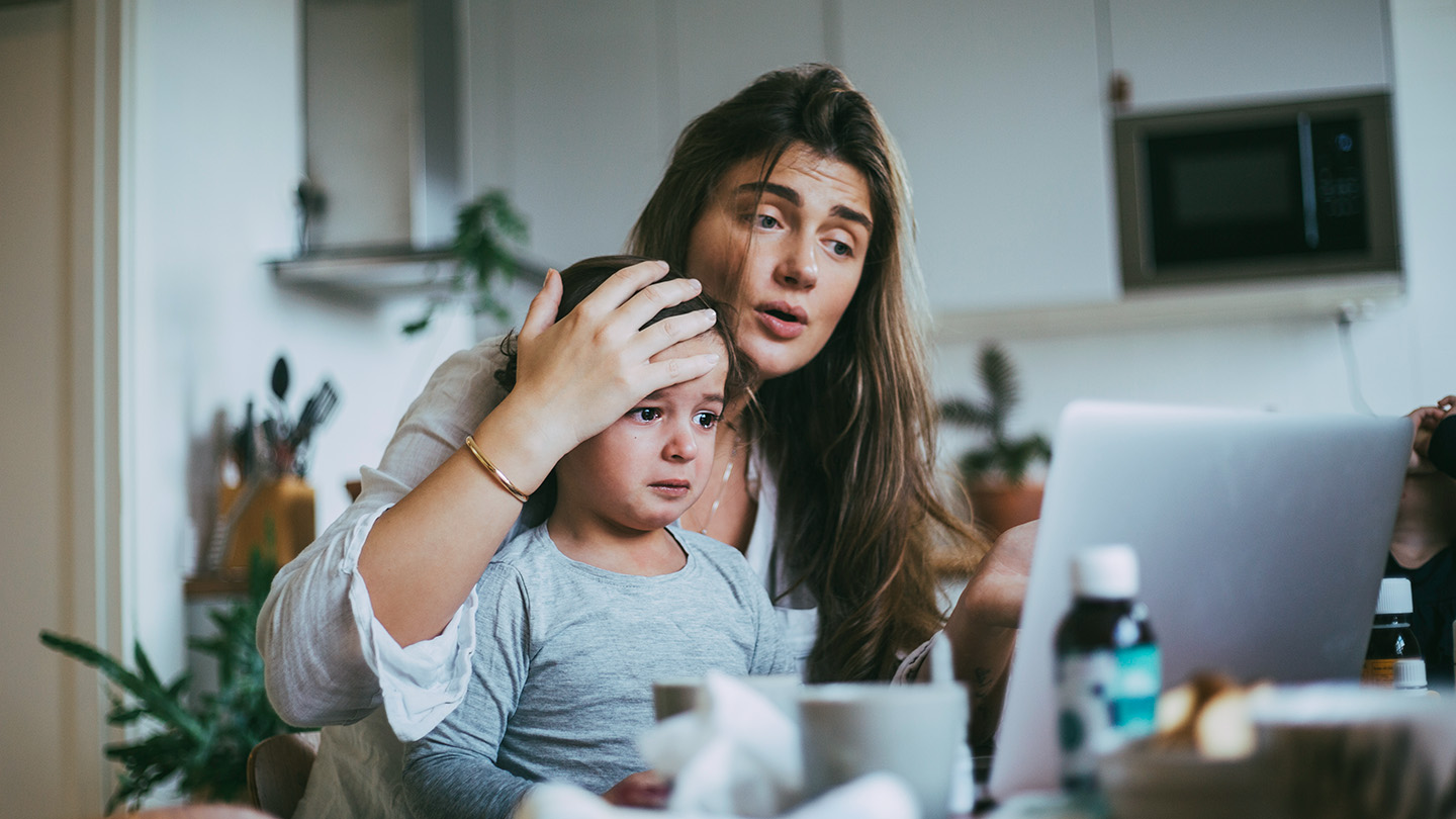 A mother holds her child's head as she appears to speak to the computer.