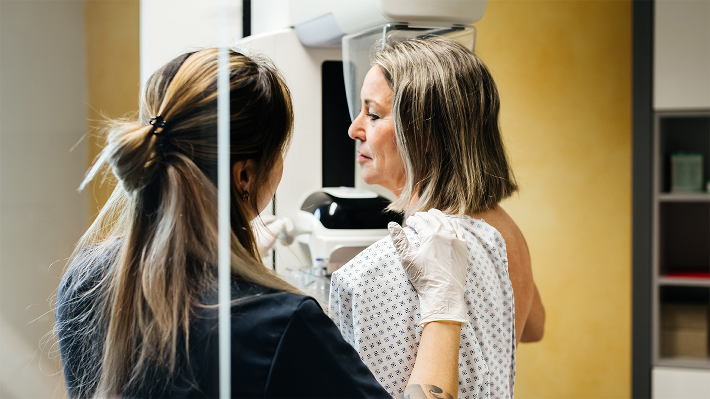 Woman in a hospital gown getting a mammography with the help of a health care worker.