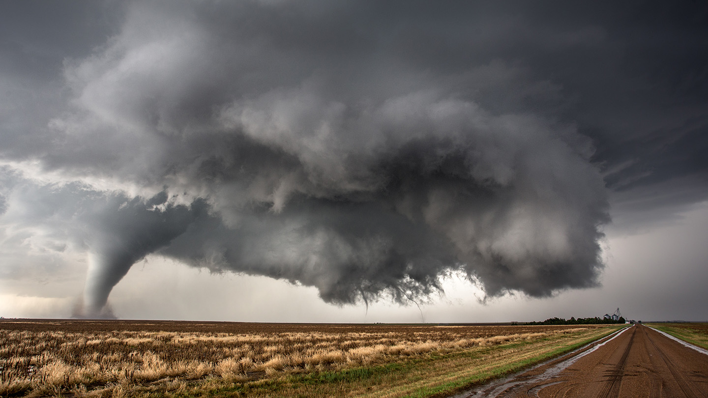 Dark storm clouds hover over a field as a large tornado touches down.