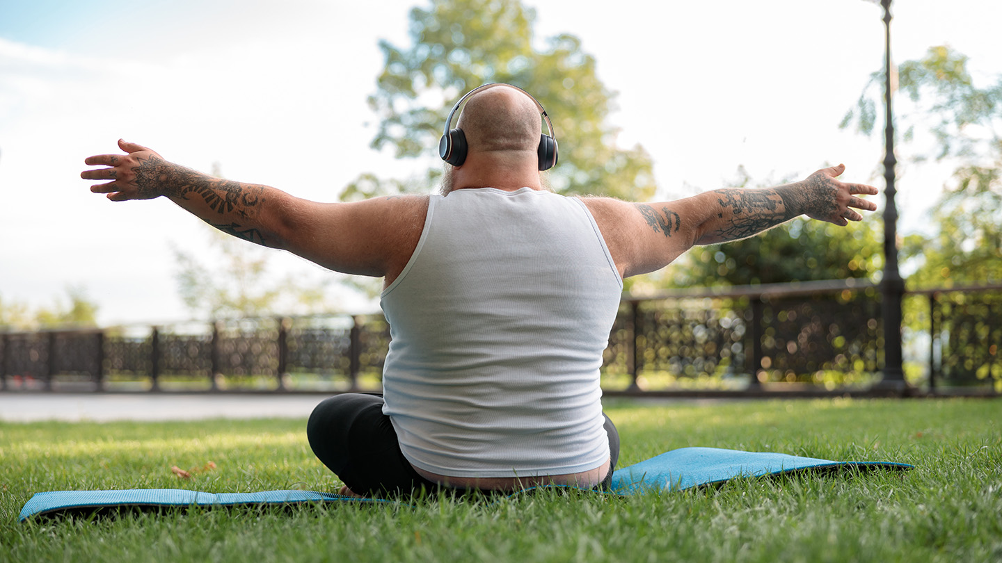 Person with arms outstretched while sitting on a yoga mat on the grass.