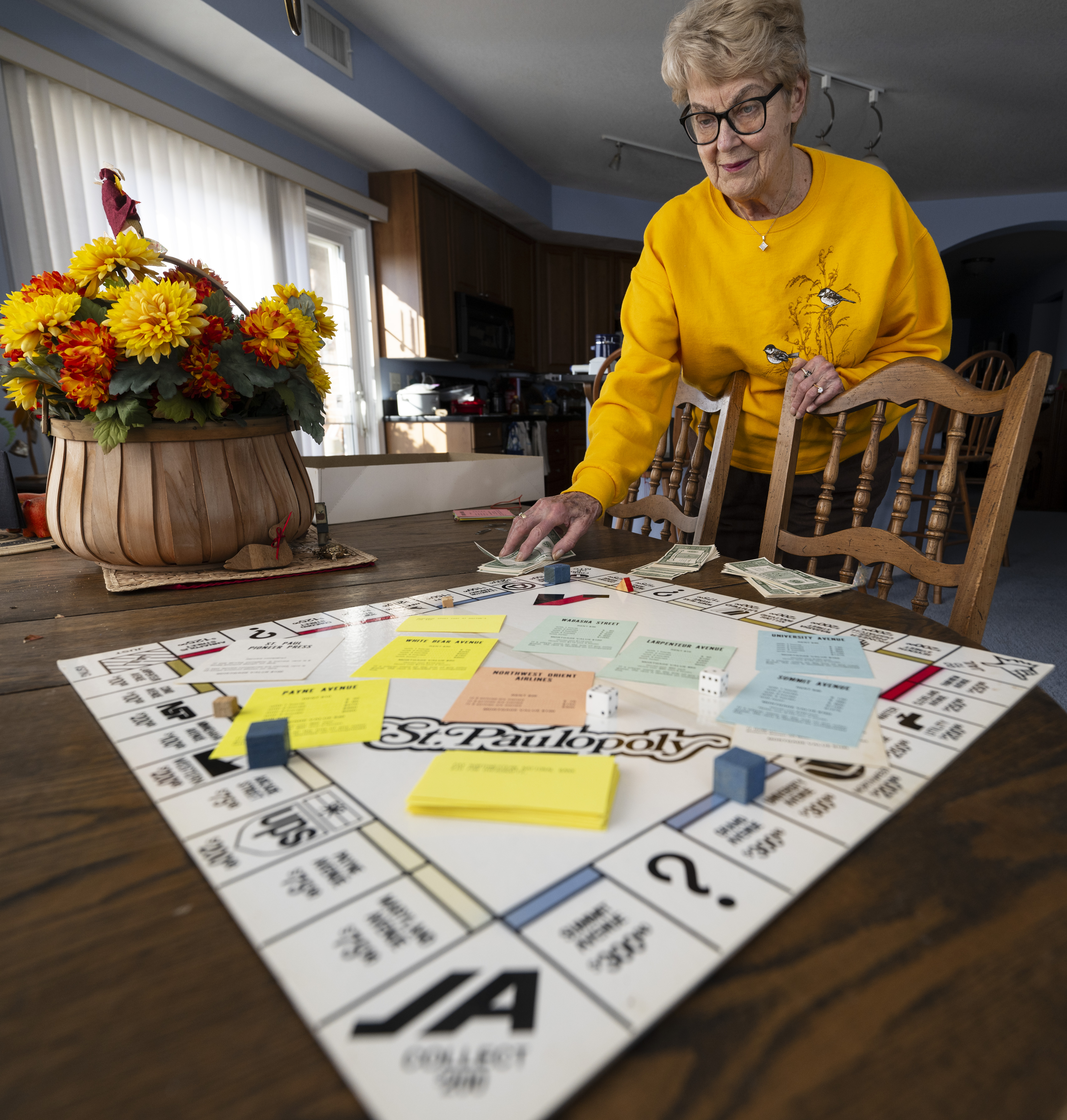 Carole Needels smiles down at a board game on her kitchen table.