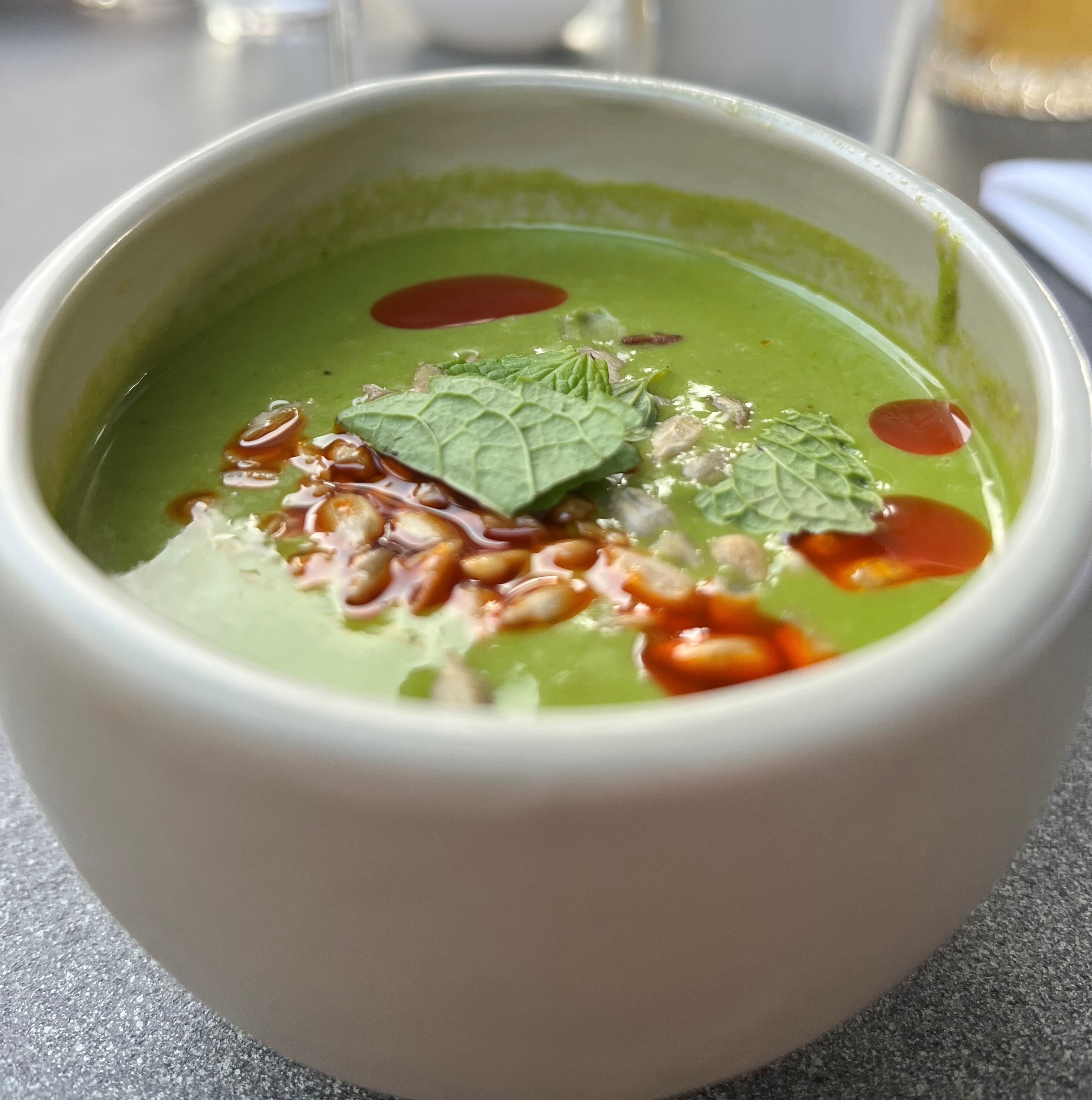 A little bowl of green gazpacho, topped with mint, chili oil and sunflower seeds