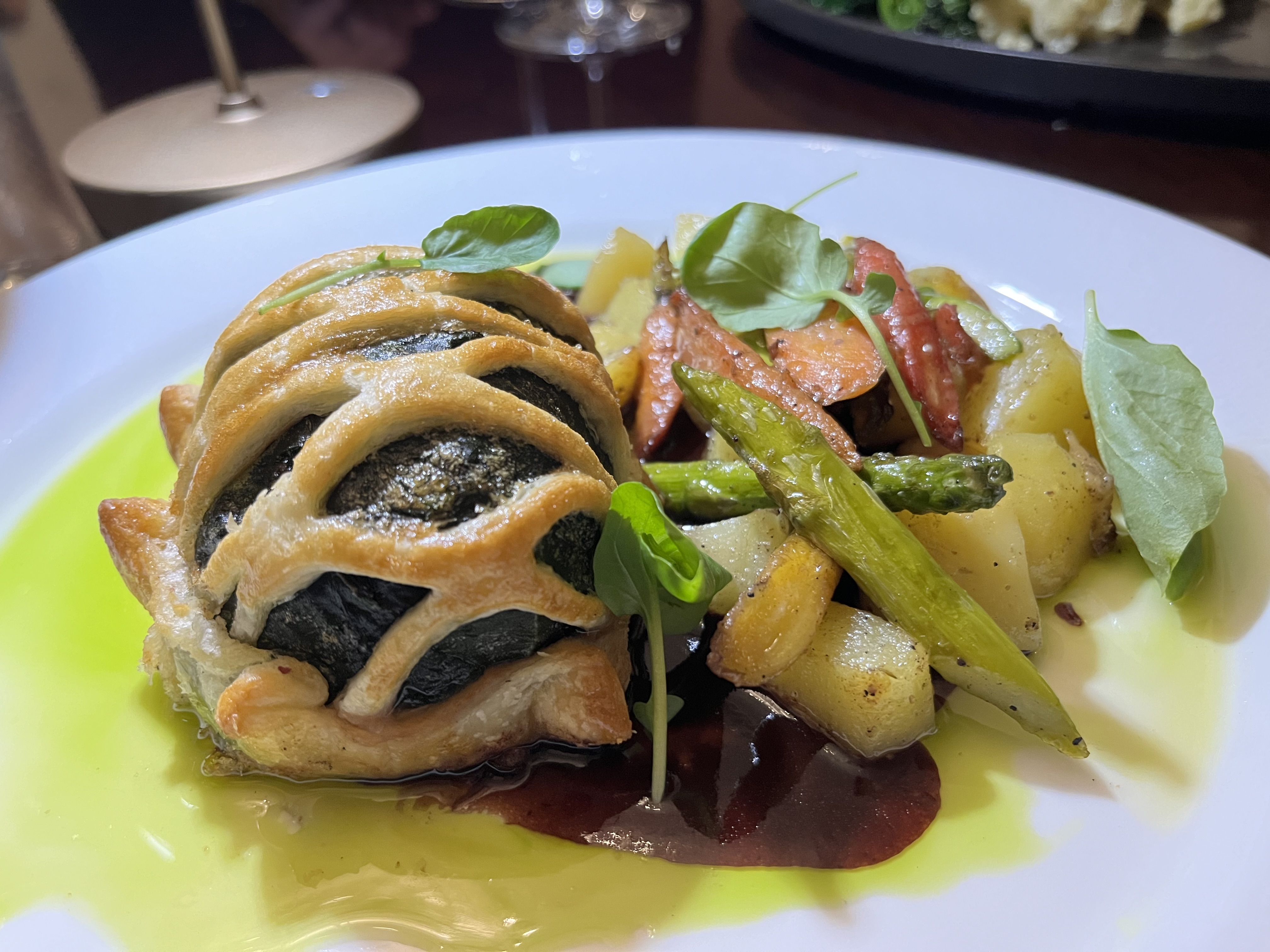 A lattice of pastry cover a hunk of beef, which is nestled next to vegetables and potatoes