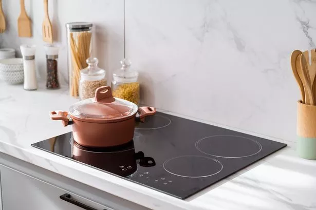 Clean new and black induction stove with control panel near marble countertop on white kitchen. Metal saucepan and jars with products on cooking surface. Cookery and homemade food concept