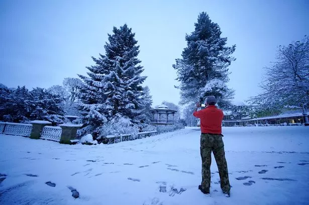 A man takes a photo of the overnight snowfall at a park in Buxton, Derbyshire