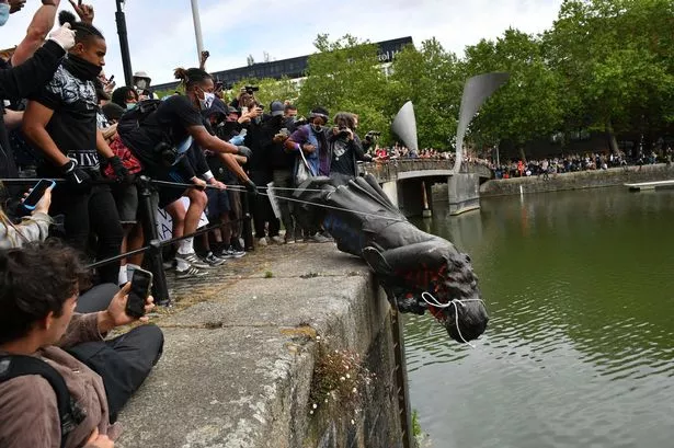 Crowd of protesters rolling statue of Edwardian man into harbour