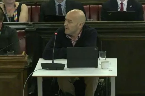 Man in a wheelchair at desk speaking into a microphone