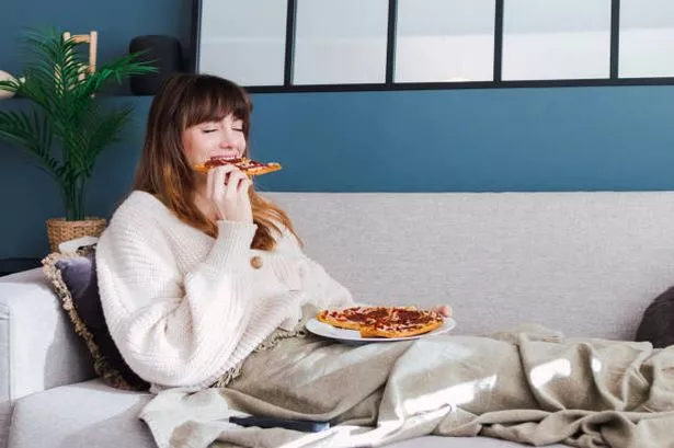 Woman sat on sofa eating pizza (stock photo)