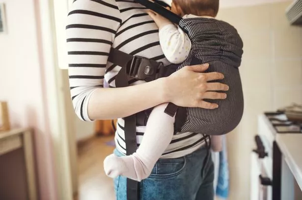 Young mother having her cute little daughter in baby carrier