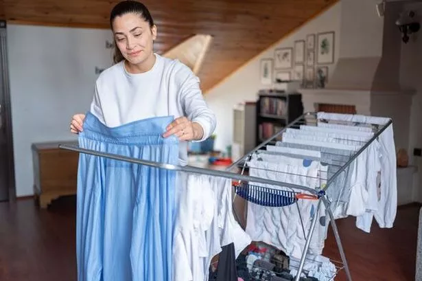 Woman-Hanging-Laundry-On-Drying-Rack-In-Room