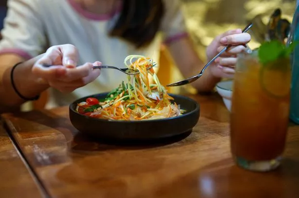 A vibrant salad, which features shredded green papaya, mango, carrots, tomatoes, peanuts, and fresh herbs