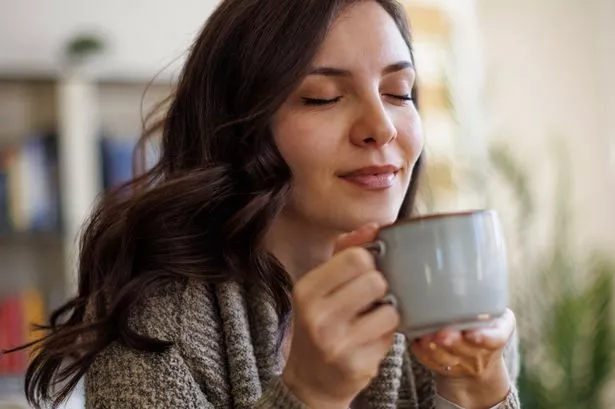 Young smiling woman enjoying in smell of fresh coffee at home